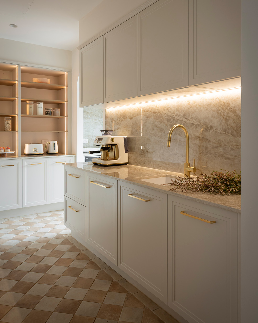 Warm white walk in butler's pantry with cleaning area, open shelving, and gold handles and tap