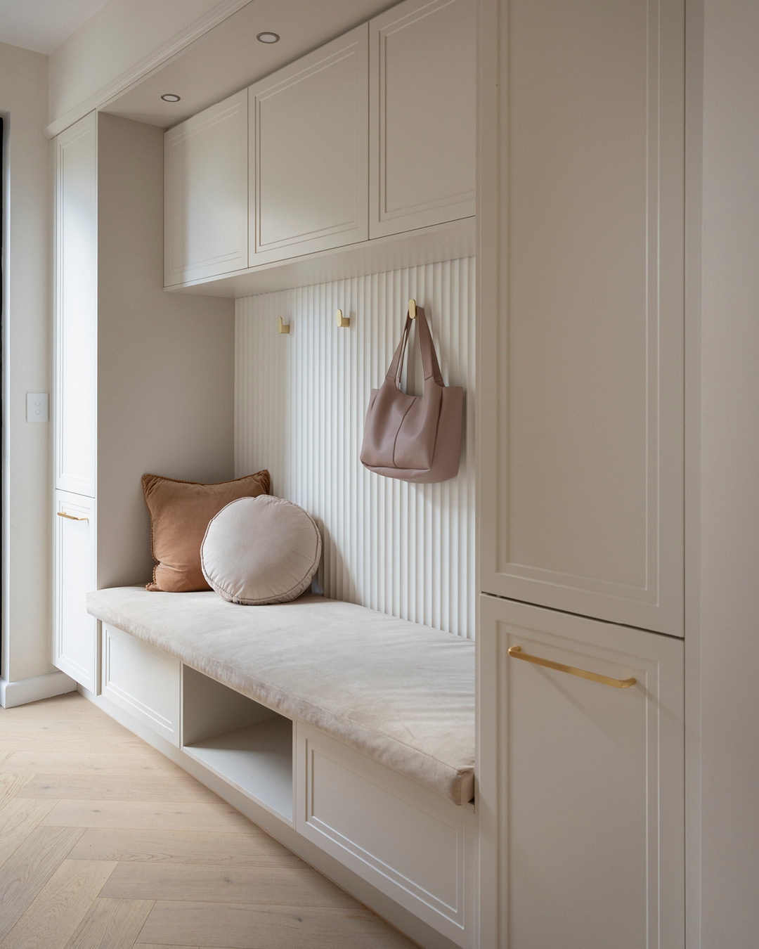 Mudroom with bench seat, storage and gold handles and hooks.