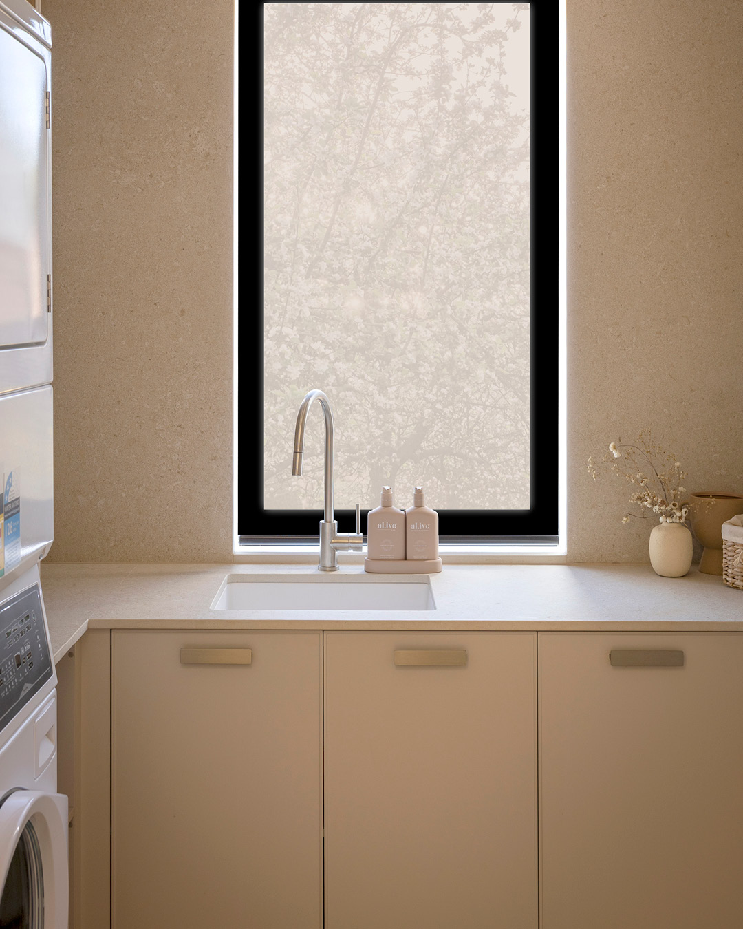 U-shaped laundry with sink and tap by a window, stacked laundry appliances and neutral cupboards