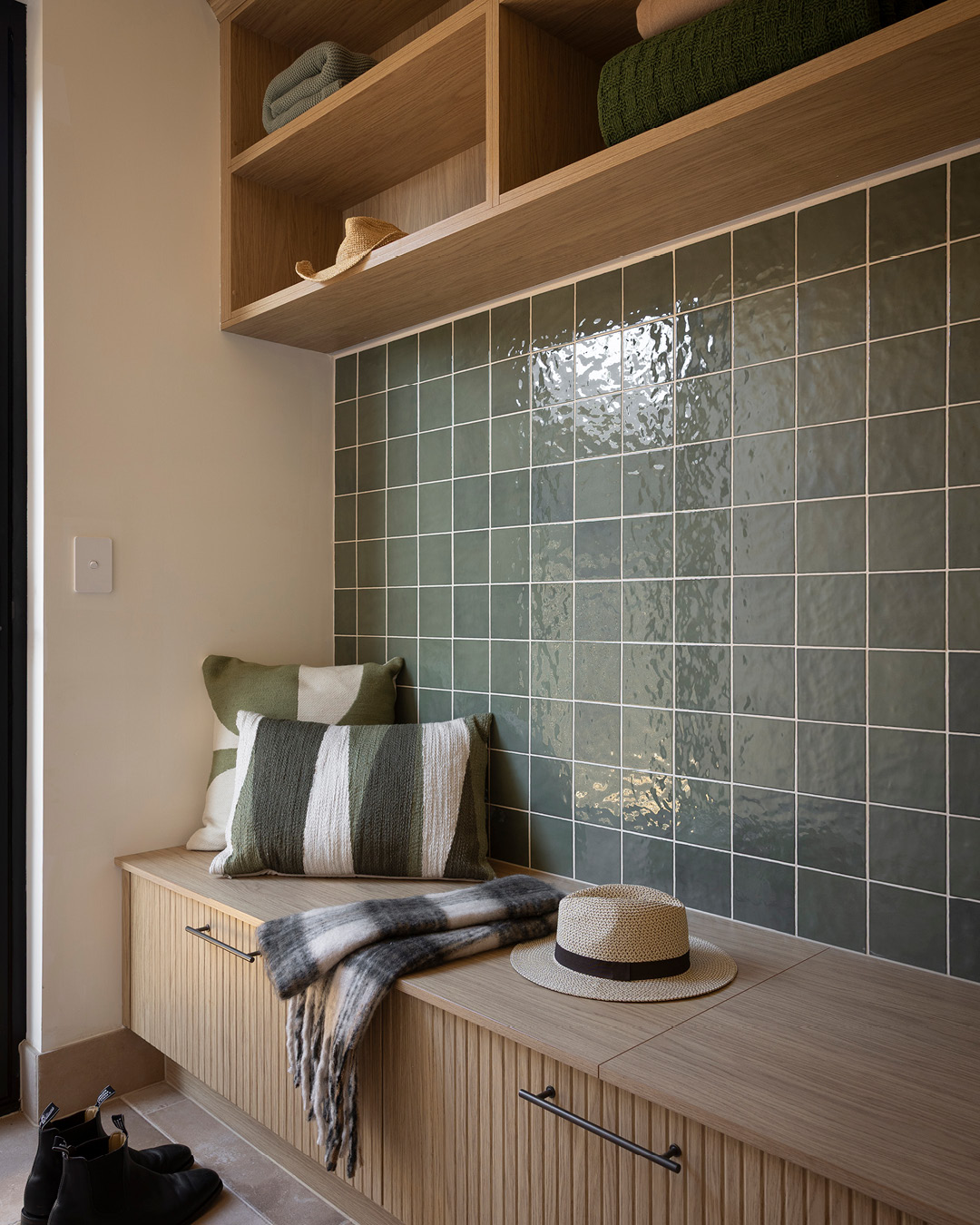 Timber-look mudroom with seating bench, drawers and green tiles.