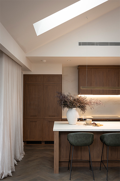 Sienna Toasted Chestnut cabinetry paired with copper-toned hardware and a marble-effect stone island creates a refined kitchen aesthetic.