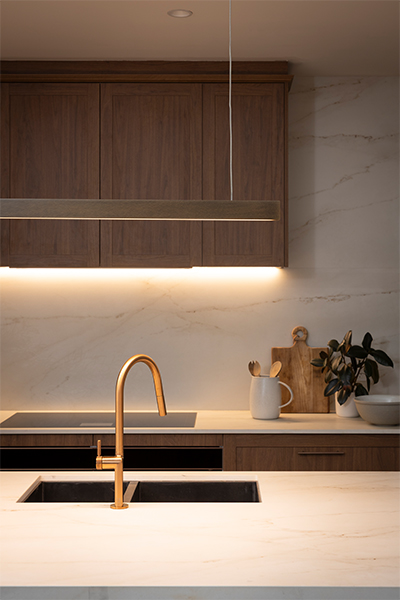 Sleek gunmetal sink and tap illuminated by flexible LED strip lighting, showcasing the warm timber and stone surfaces nearby.