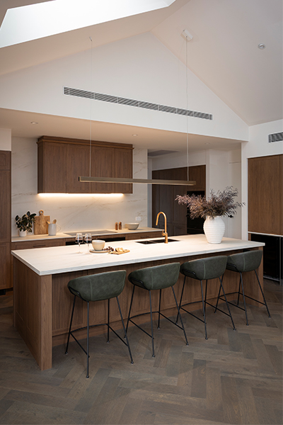 Warm and inviting kitchen featuring timber-toned cabinetry, copper bronze handles, and a striking central island benchtop.