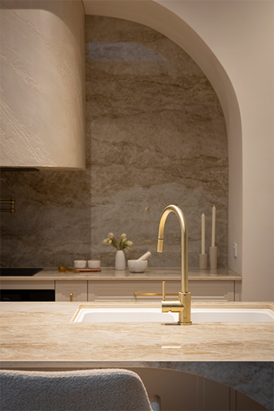 Double undermount white quartz sink with gold gooseneck mixer tap and pull-out sprayer, highlighted by ambient lighting.