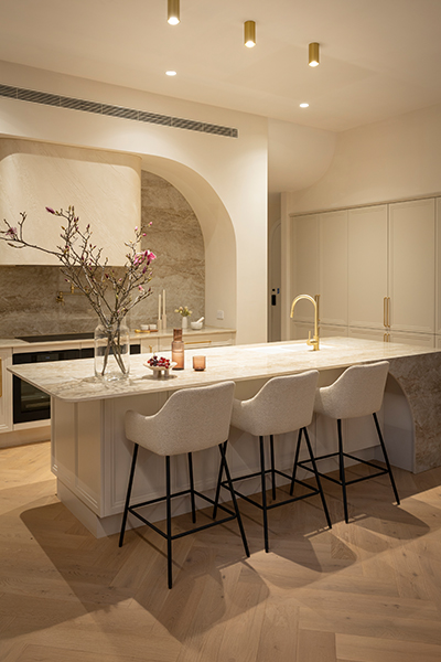 Chic contemporary kitchen featuring soft curves in the island, splashback, and bulkhead, with a warm palette of white tones with gold accents such as handles.