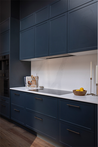 White and Baltic Blue kitchen featuring a sleek cooktop, integrated rangehood, and layered stone benchtops for a modern farmhouse look.