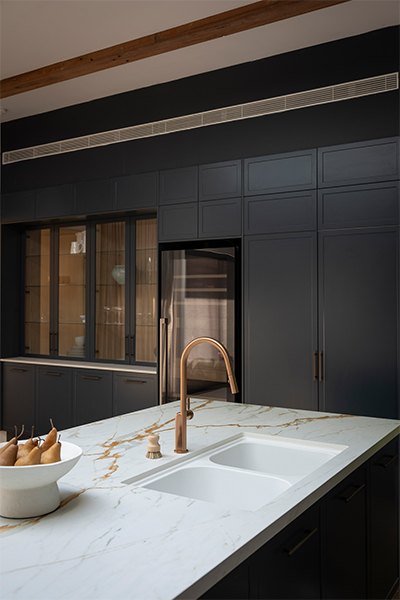 Close-up of white Häfele quartz sink, complemented by a sleek copper tap, within the bold blue and gold kitchen.