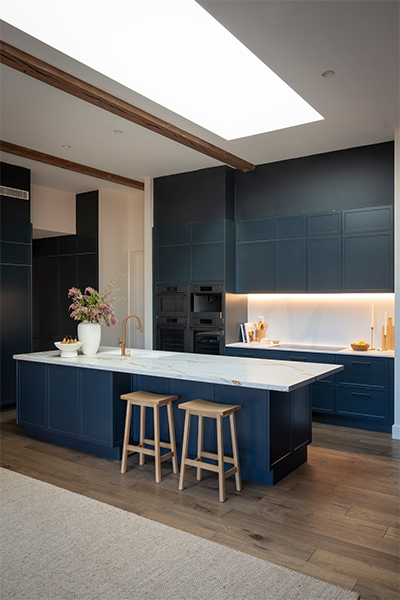 L-shaped kitchen with Sierra IV Baltic Blue cabinetry, layered benchtops in Dekton Reverie and Xeron Cascade Gold, and Choco Bronze handles.